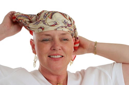 A beautiful woman, bald from chemotherapy,  prepares to remove the scarf covering her head.  